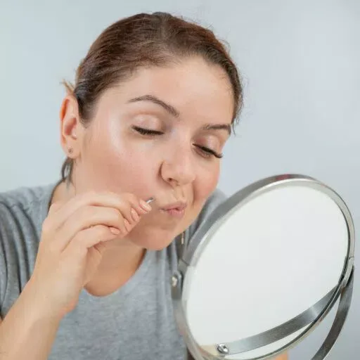 Femme se regardant dans un miroir de table pour s'épiler les poils du visage à la pince à épiler